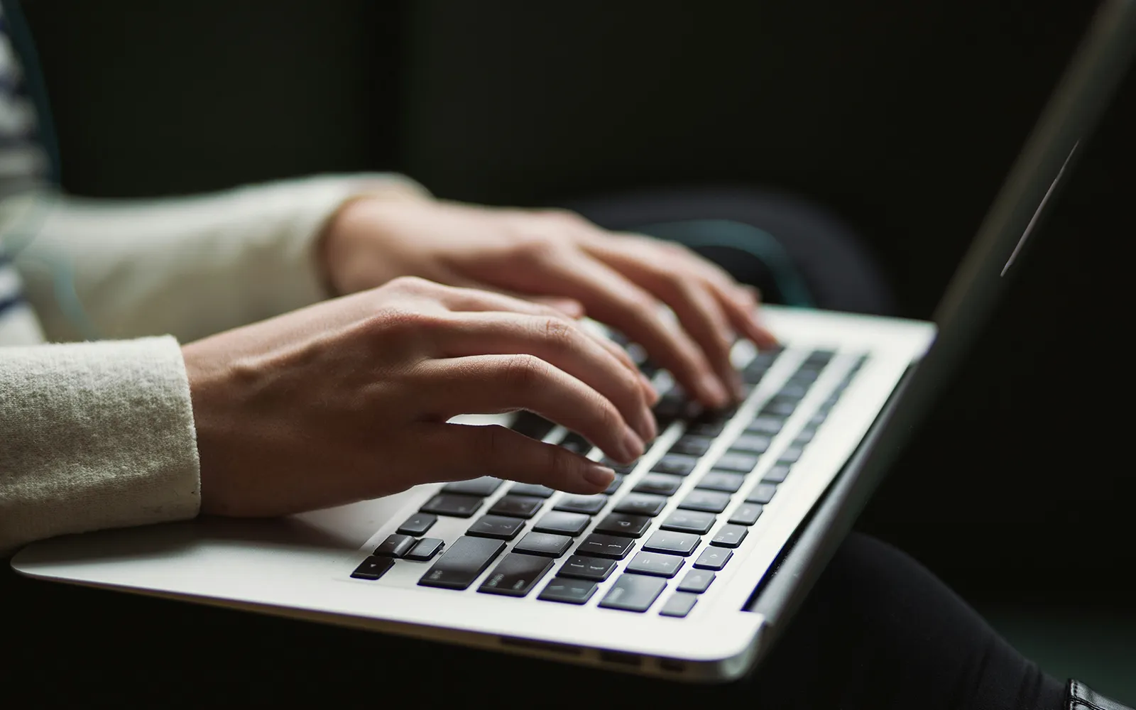 Close-up of hands typing on a keyboard against a dark background